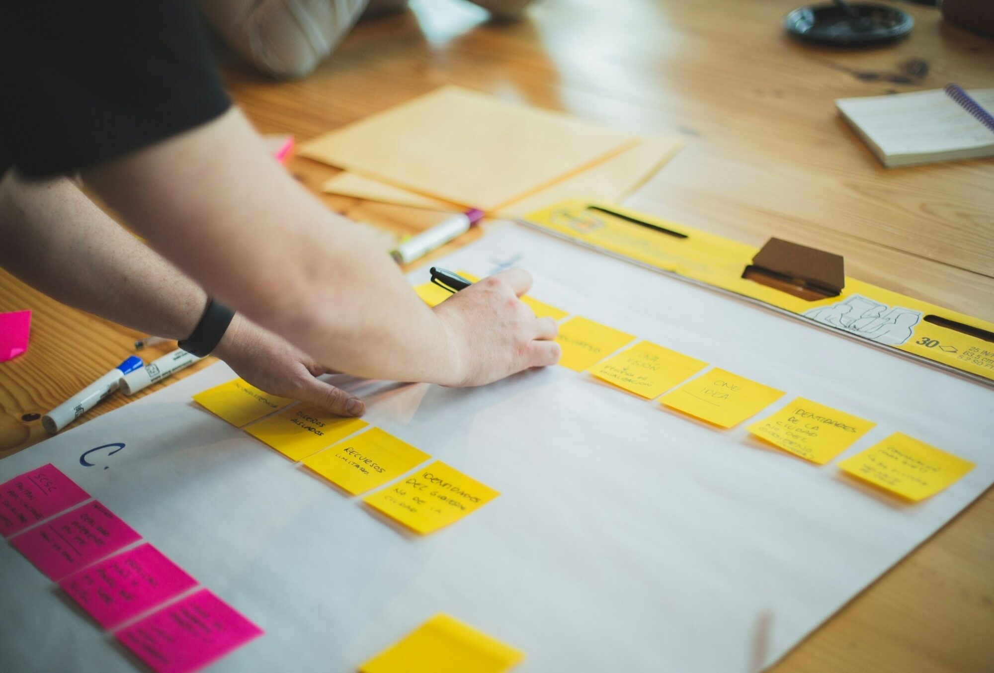 A person's hand writing on a series of fluorescent orange and pink sticky notes
