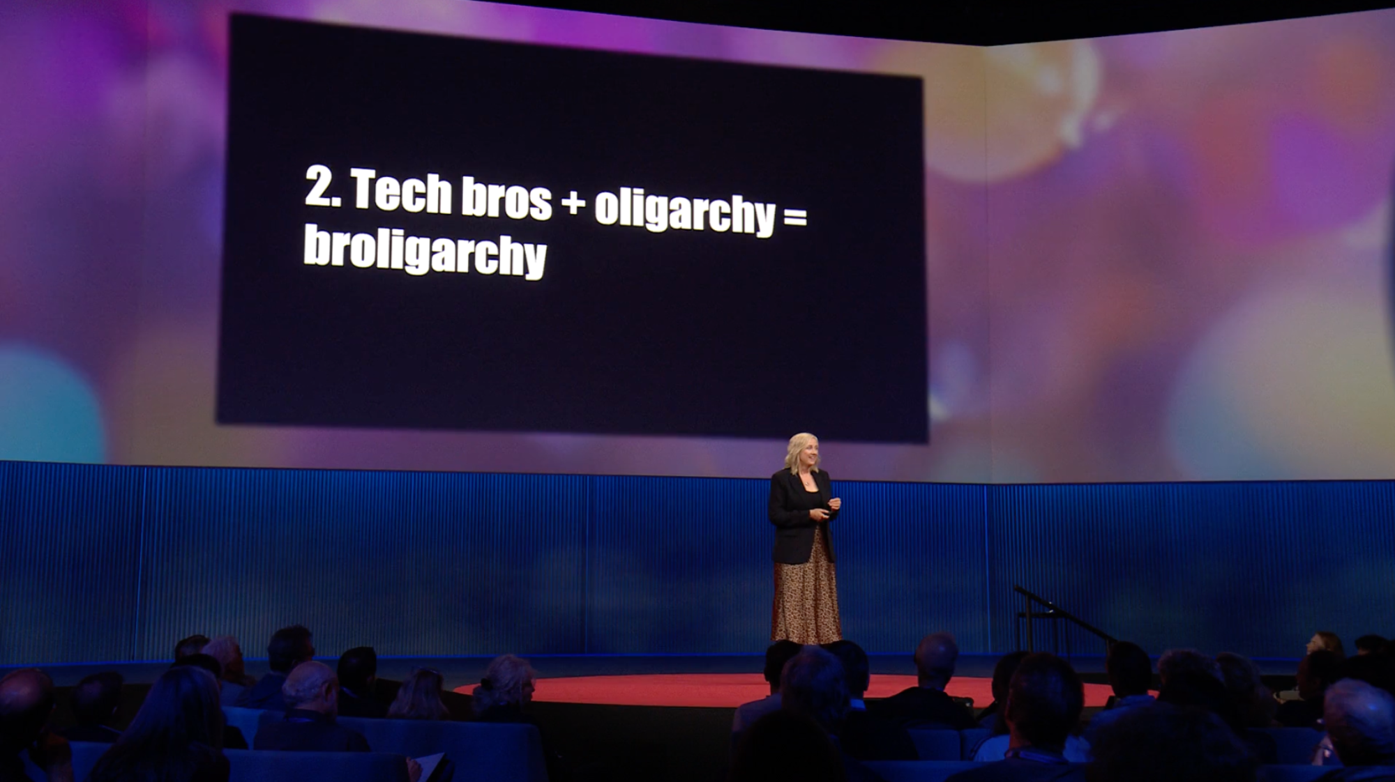 Carole Cadwalladr standing on a stage, addressing an audience, in front of a slide that says "Tech bros plus oligarchy equals broligarchy"